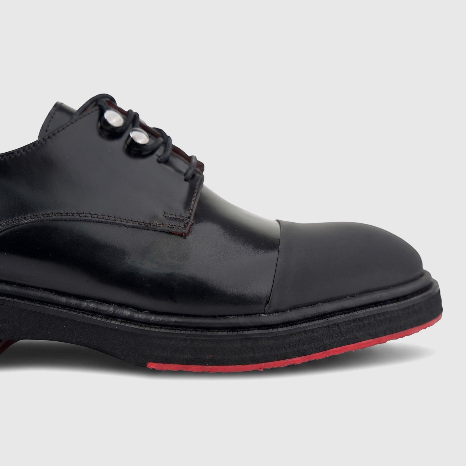Close-up of a black leather men's formal lace-up shoe with a chunky sole and red accents, viewed from the side.