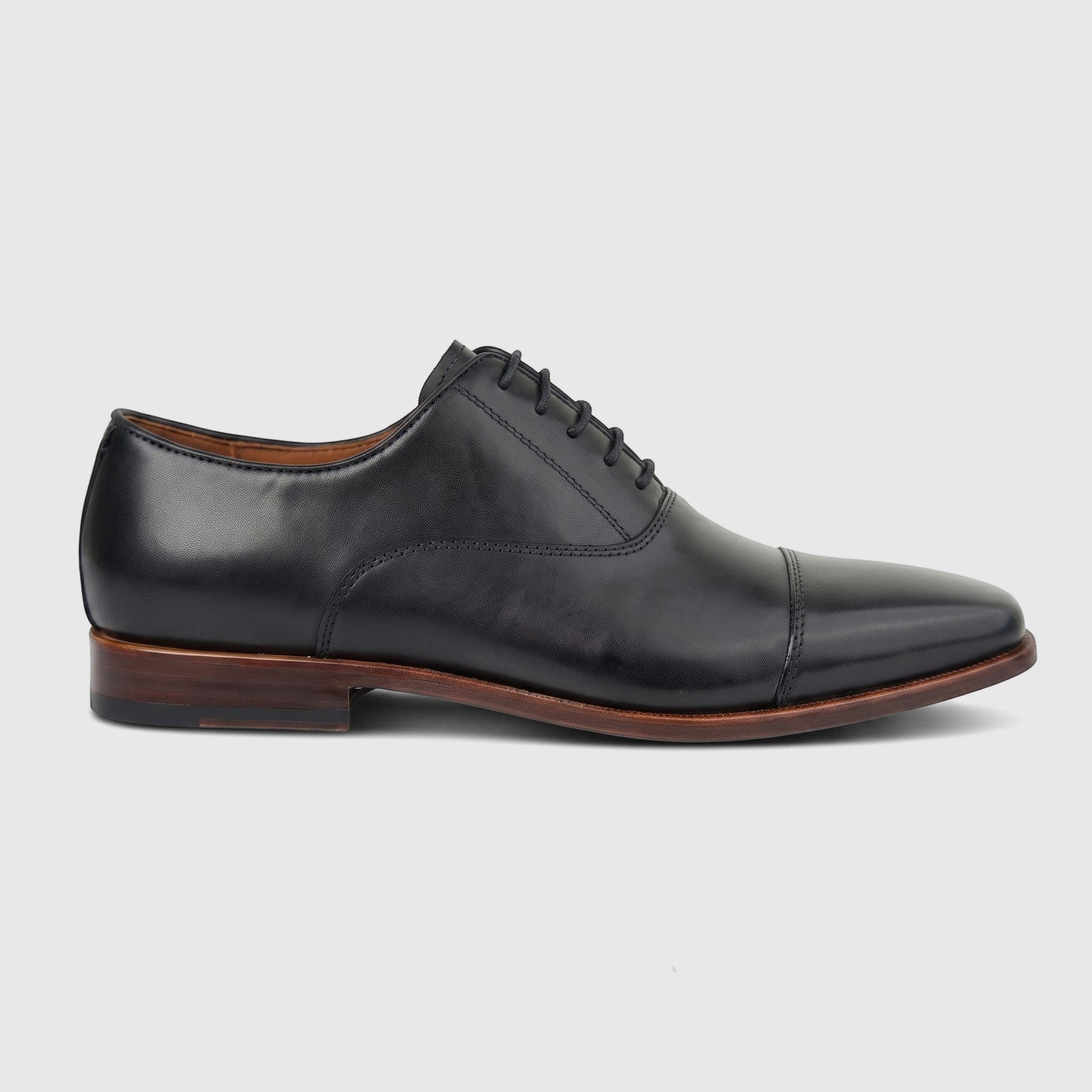 Black leather men's dress lace-up shoe with a cap toe and brown sole, viewed from a side profile on a white background.