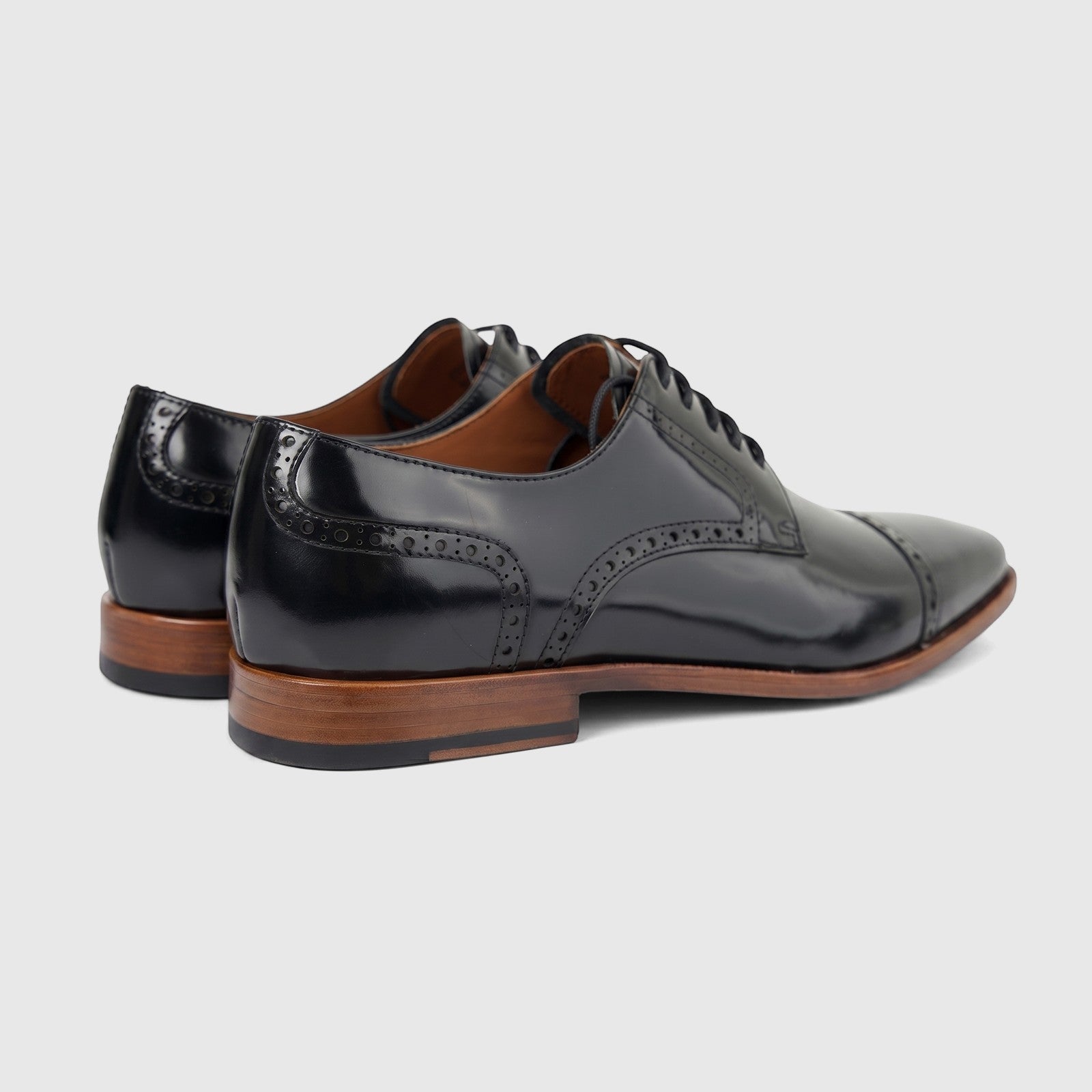 A pair of glossy black leather men's dress shoes with lace-up closure and brogue detailing, showcasing a cap toe and a brown