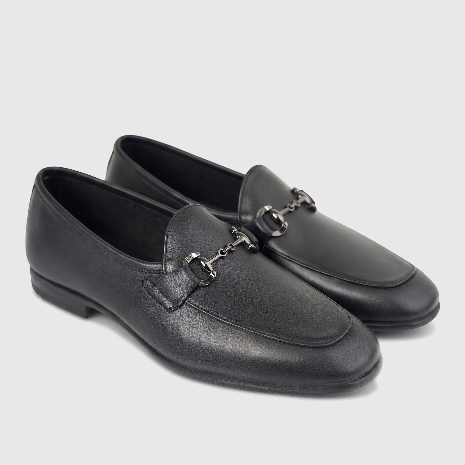 A pair of black leather men's loafers with a silver-toned metal horsebit detail, shown from a side angle.