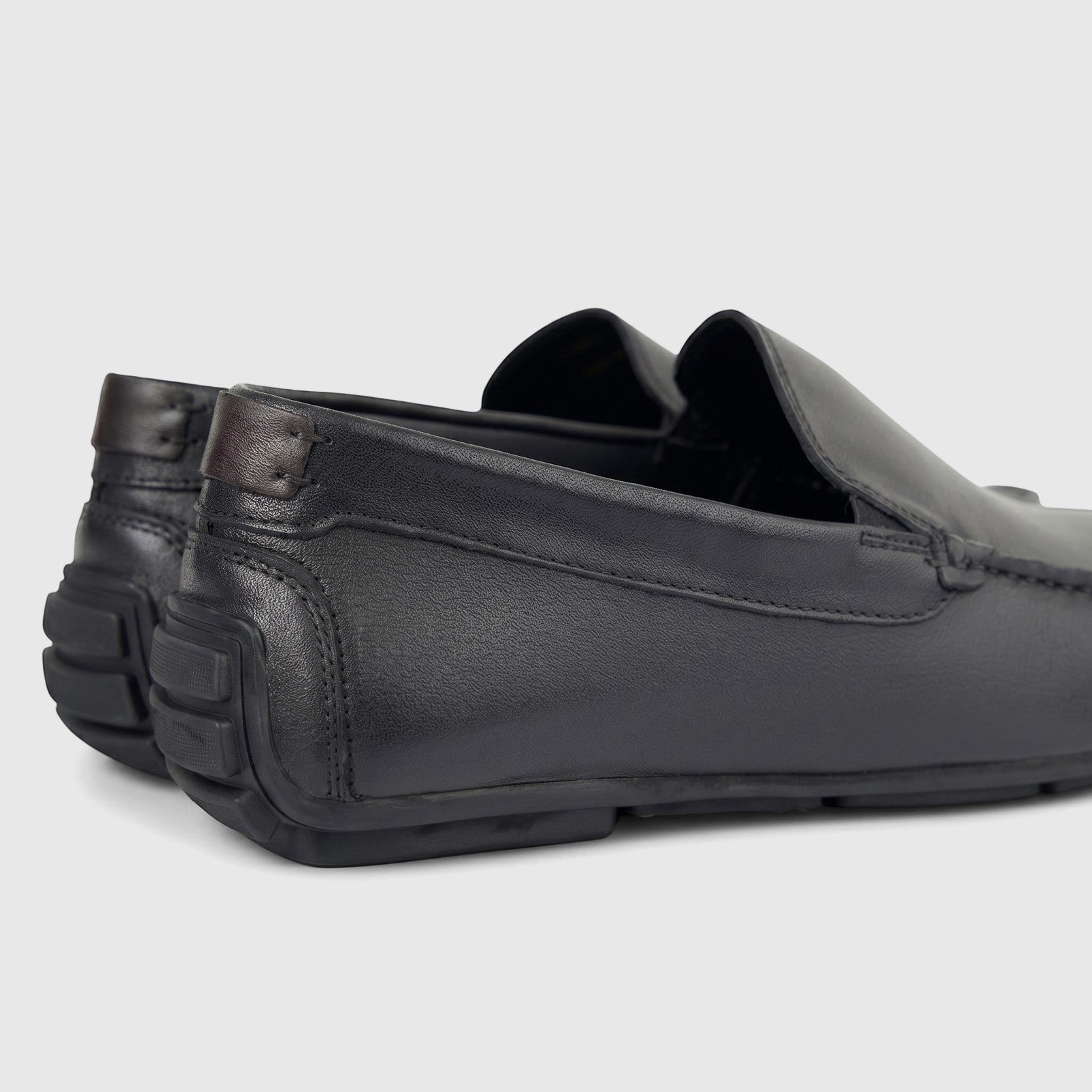 A pair of black leather men's loafers with visible stitching and textured heel details, presented from a side-rear angle on