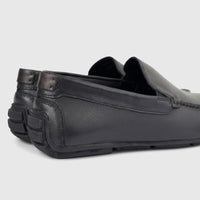 A pair of black leather men's loafers with visible stitching and textured heel details, presented from a side-rear angle on