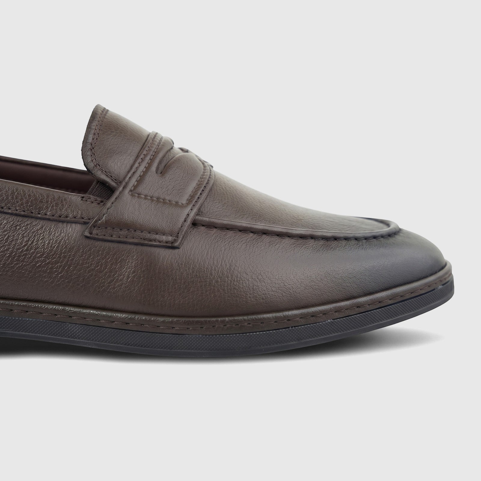 A close-up of a brown leather men's loafer from the side, showcasing its textured surface and classic design.
