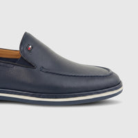 Navy leather men's loafer with a small rectangular logo and a white and blue striped sole, presented in a close-up side view.