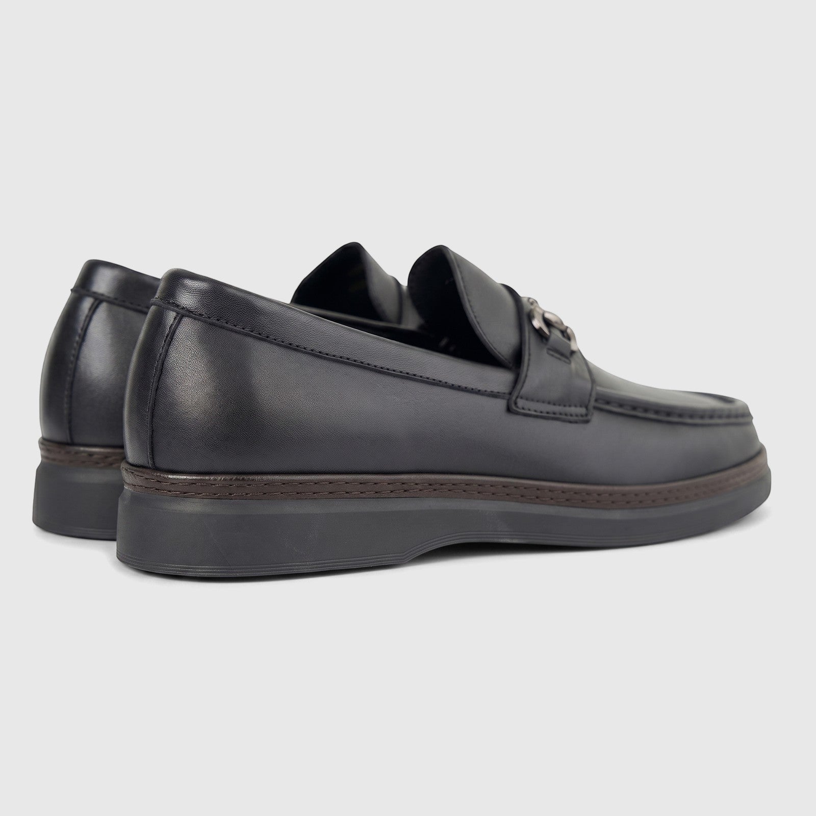 A pair of black leather men's loafers with metal horsebit detailing, viewed from a side-rear angle, on a white background.