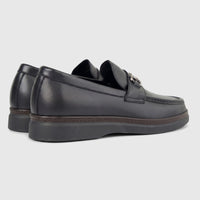 A pair of black leather men's loafers with metal horsebit detailing, viewed from a side-rear angle, on a white background.