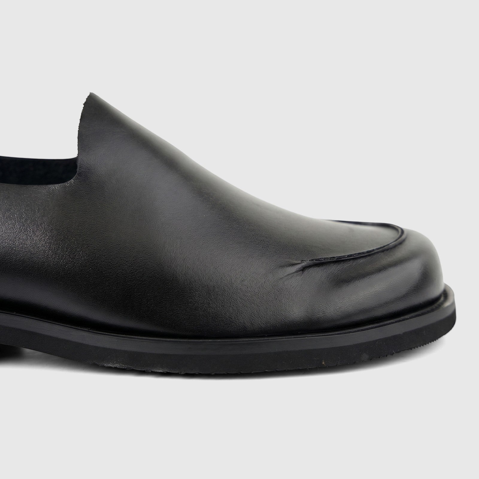 Close-up view of a black leather Formales Men's Slip On shoe, highlighting the classic moc-toe stitching and smooth finish.