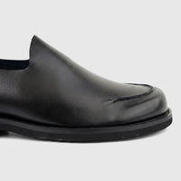 Close-up view of a black leather Formales Men's Slip On shoe, highlighting the classic moc-toe stitching and smooth finish.