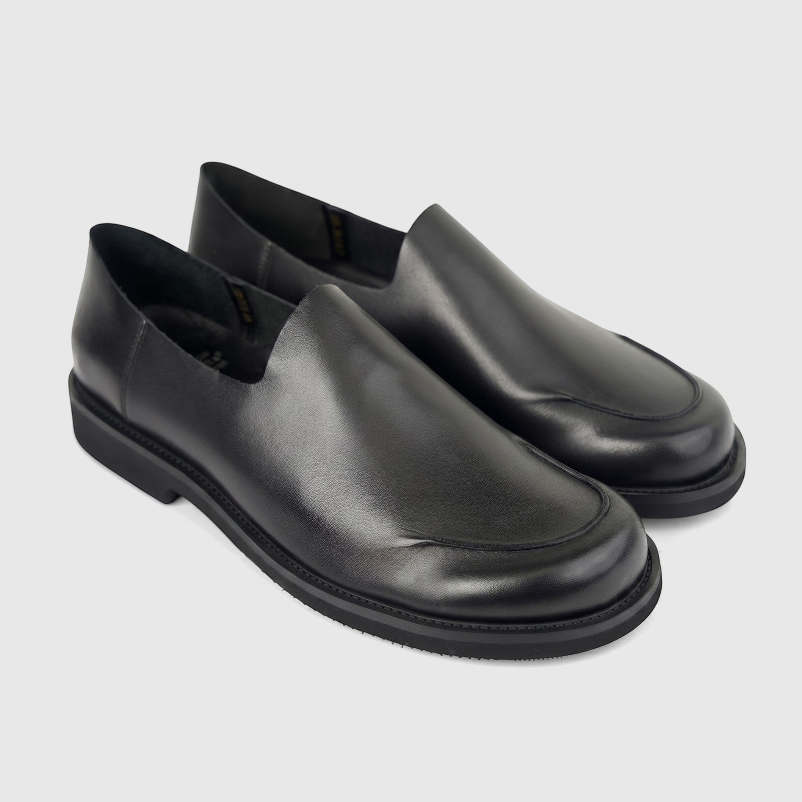 A pair of Formales black leather men's slip-on shoes, showcasing prominent toe stitching and thick soles, on a white