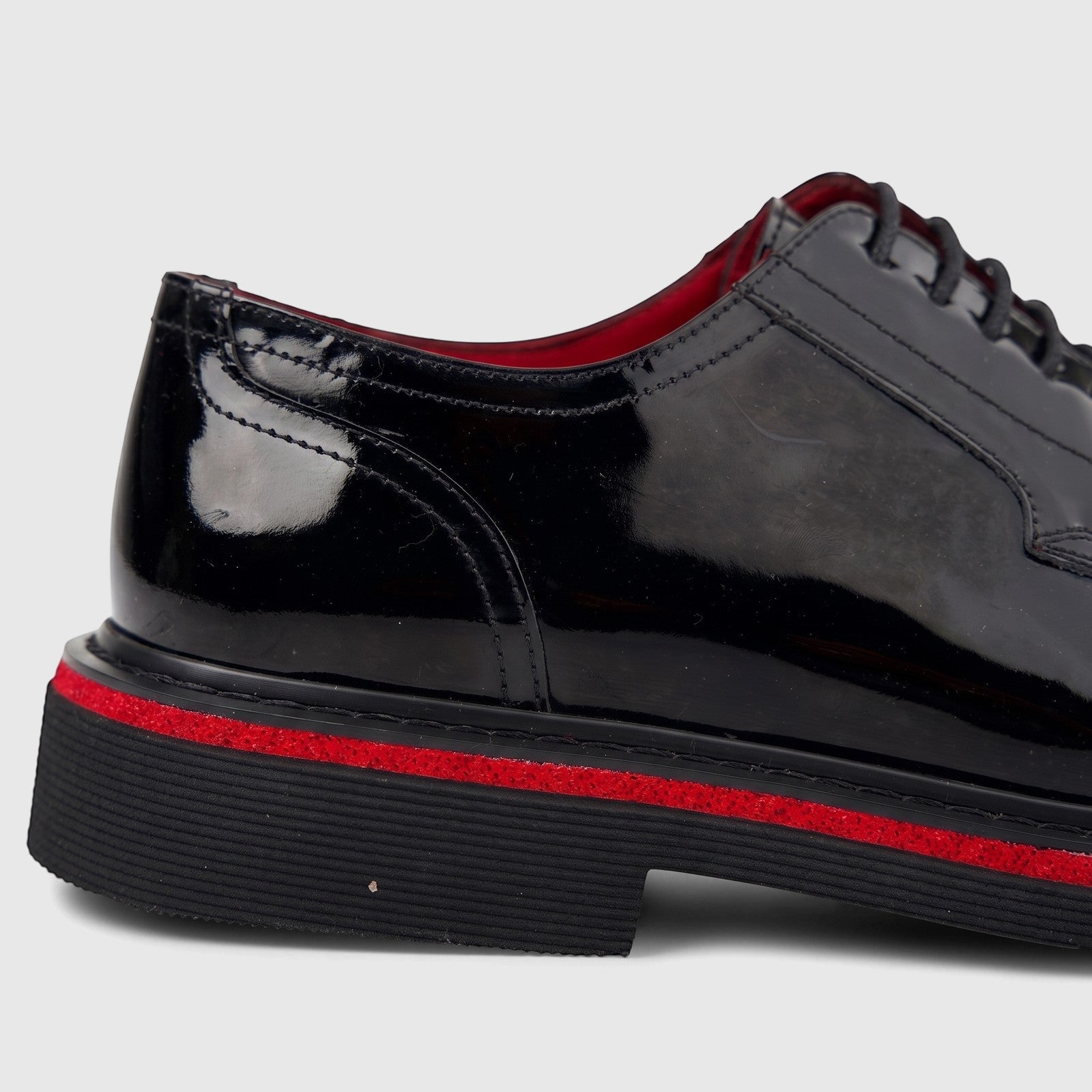 Black patent leather men's formal lace-up shoe with a chunky black sole and a distinctive red stripe.