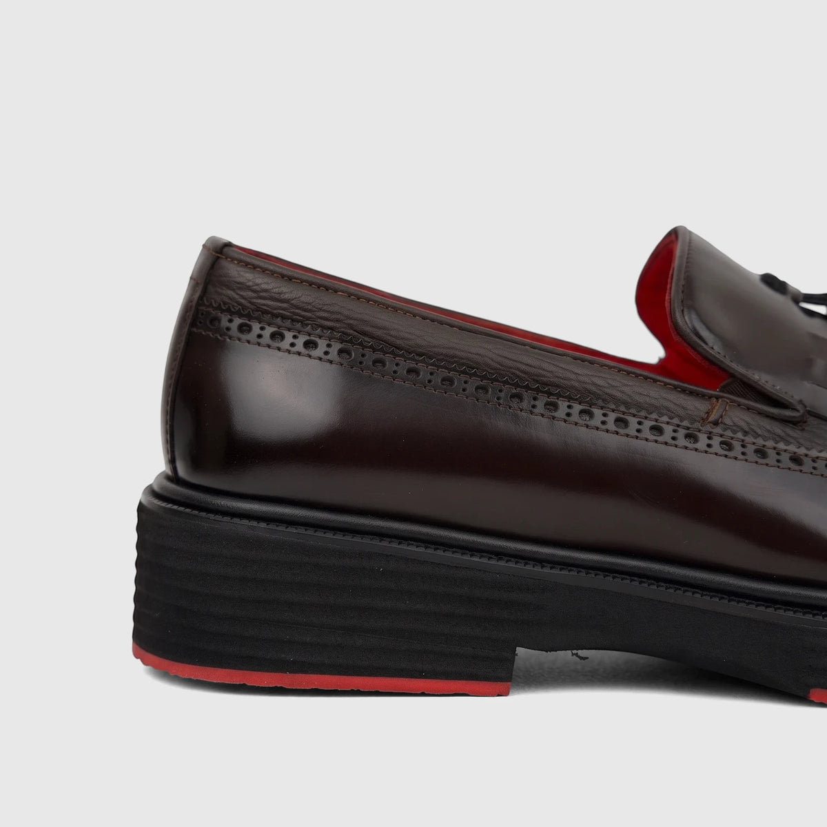 Formales Unisex dark brown leather loafer with chunky black sole, red accent, brogue details, and tassels, side view.