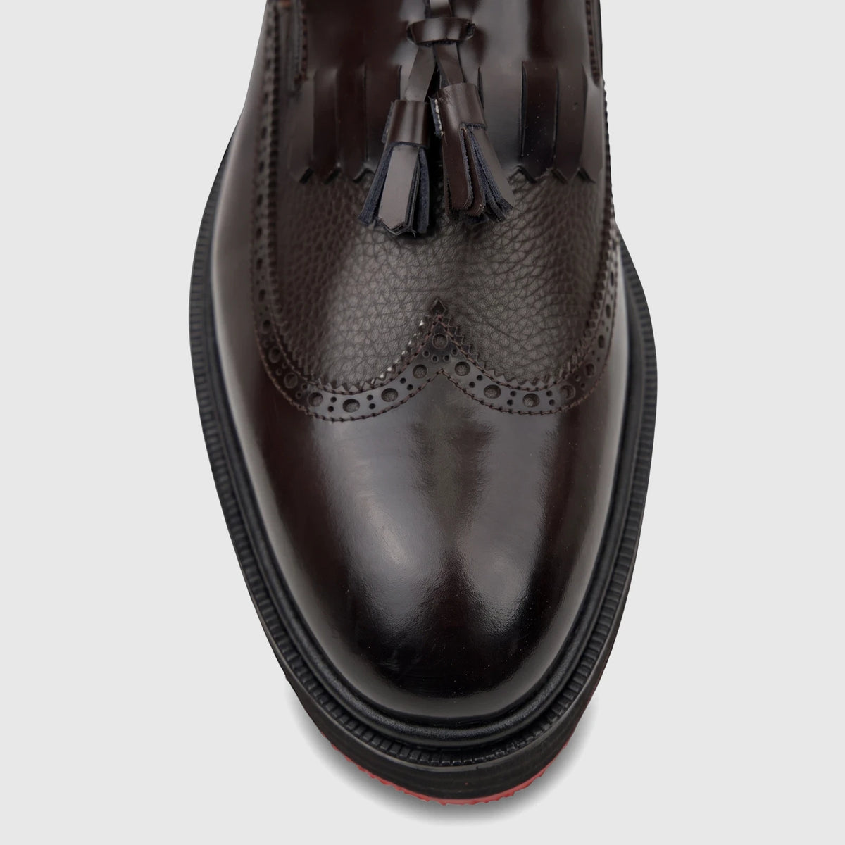Close-up top view of a dark brown leather chunky sole loafer with brogue detailing and decorative tassels, suitable for