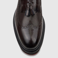 Close-up top view of a dark brown leather chunky sole loafer with brogue detailing and decorative tassels, suitable for