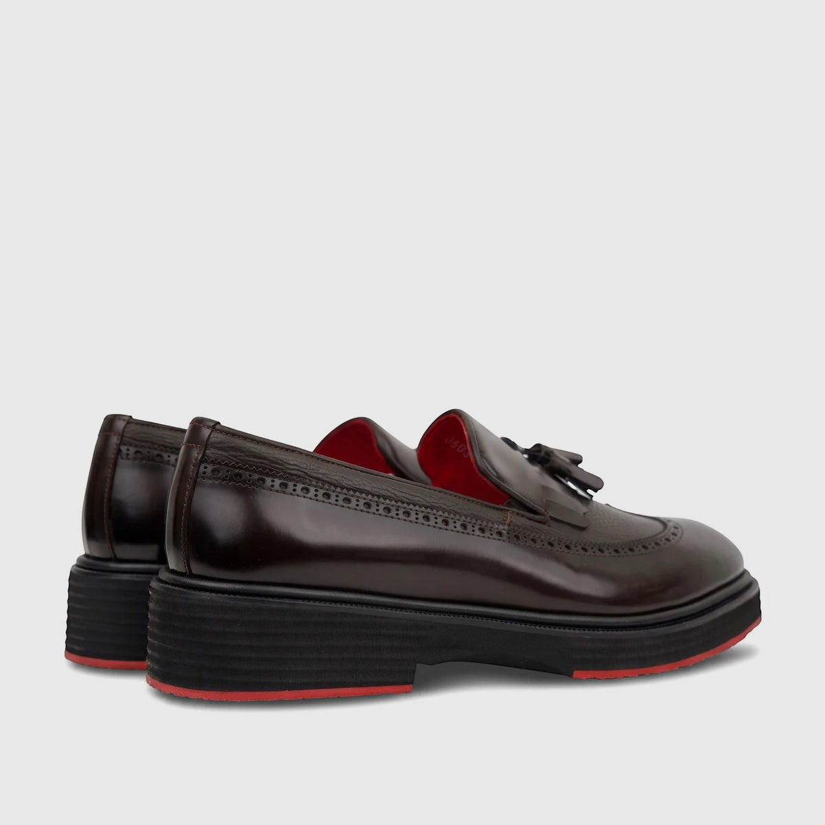 Brown leather chunky sole loafers with brogue details, tassels, and red accents, presented in a side and back view.