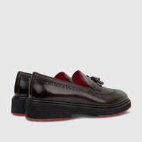 Brown leather chunky sole loafers with brogue details, tassels, and red accents, presented in a side and back view.