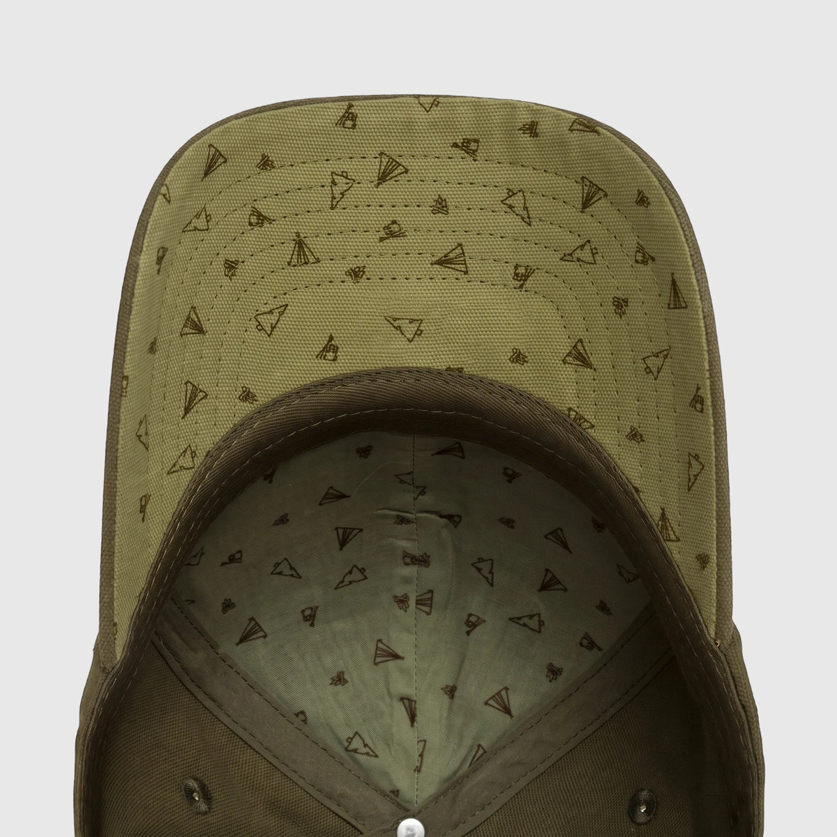 Green cap, underside view, with a geometric tent pattern on the brim and inner crown. Shows detailed stitching and two metal