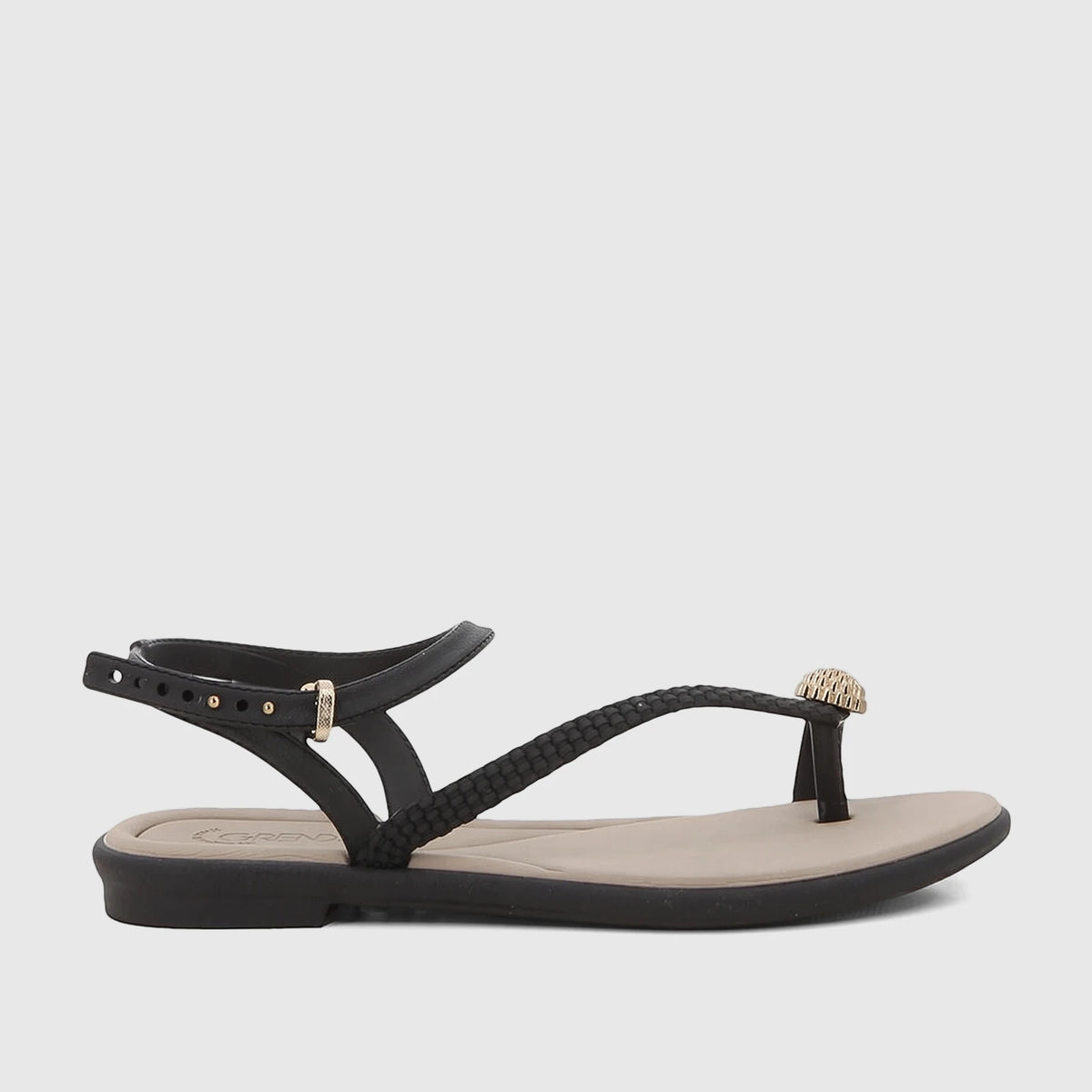 Black Grendha Icone flat sandals featuring an ankle strap, braided front, and a gold toe post detail, shown in side view.