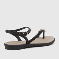 Black Grendha Icone sandal with an ankle strap, thong style, and gold buckle detail, shown from a side view.