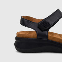 Close-up side view of a black HP Ladies Comfort Sandal Saria, featuring black straps, a tan footbed, and a thick black