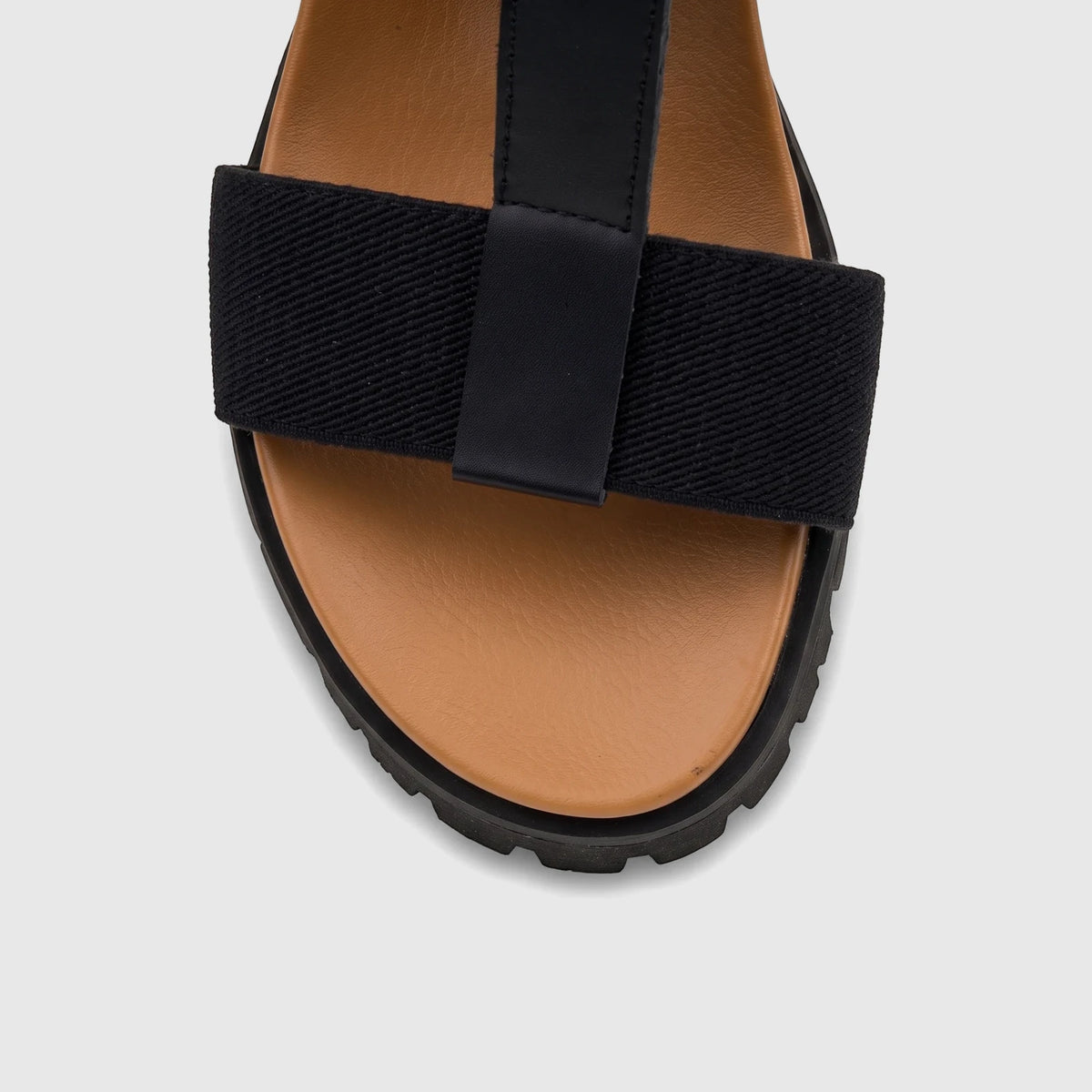 A close-up view of a black and tan HP Ladies Comfort Wedge Sandal with elastic and T-straps, and a thick black sole.