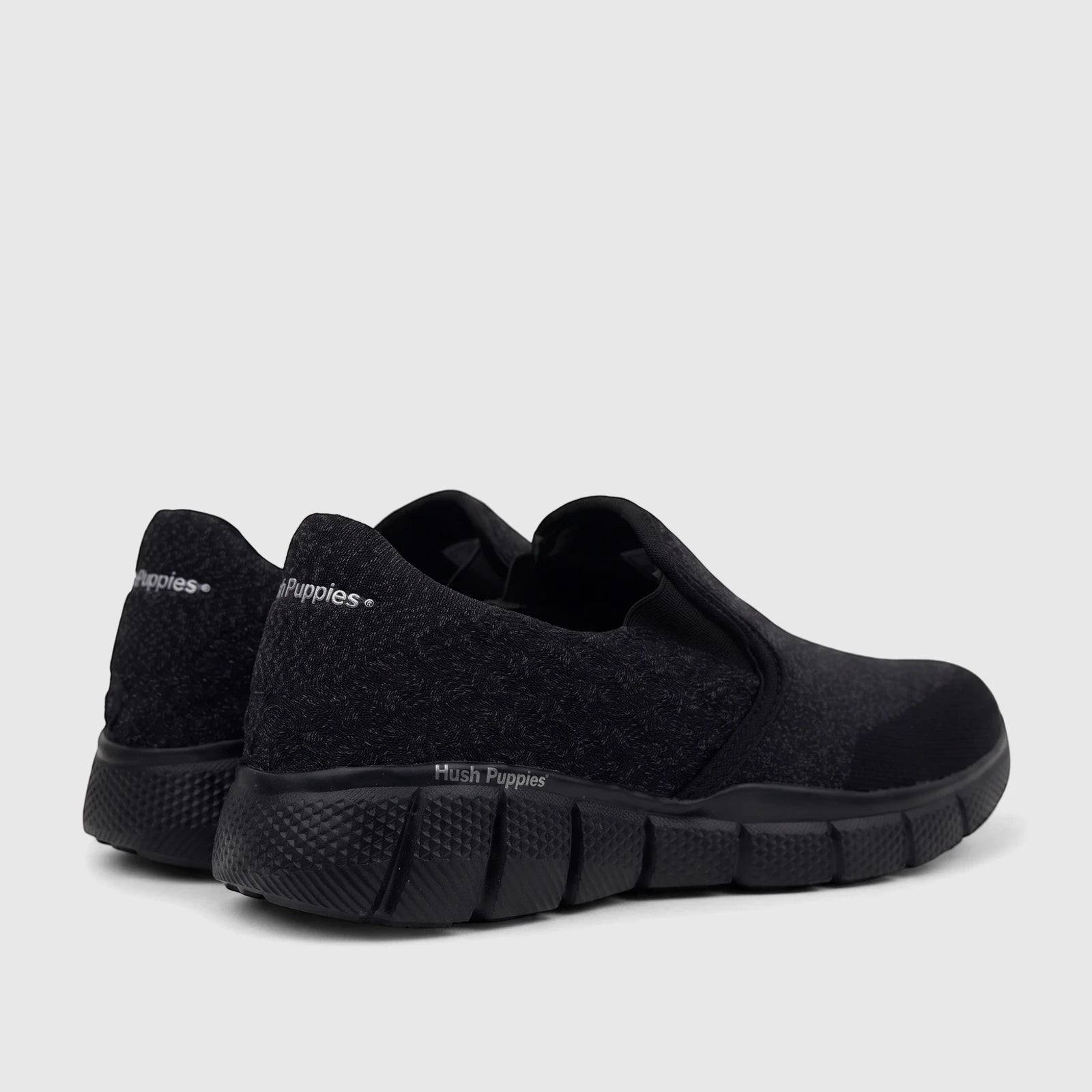Rear quarter view of a pair of black HP Men's Comfort Slip On Sneakers, showcasing their knit texture and cushioned soles.