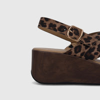 Close-up of a leopard print wedge sandal with a gold buckle and dark wood-effect platform sole.