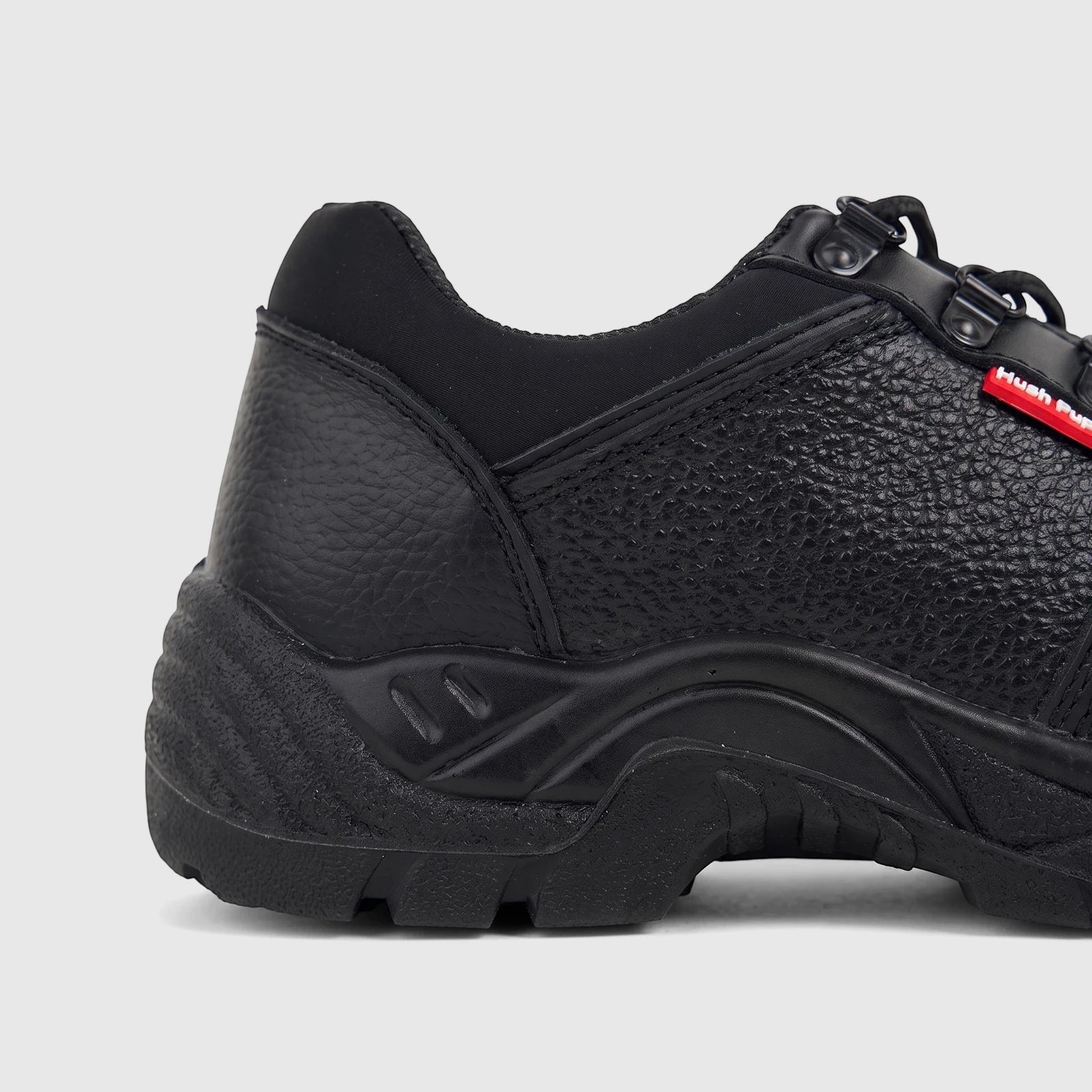 HP Unisex black safety lace-up steel toe shoe, made of textured leather, seen from a side view showcasing the heel and Hush