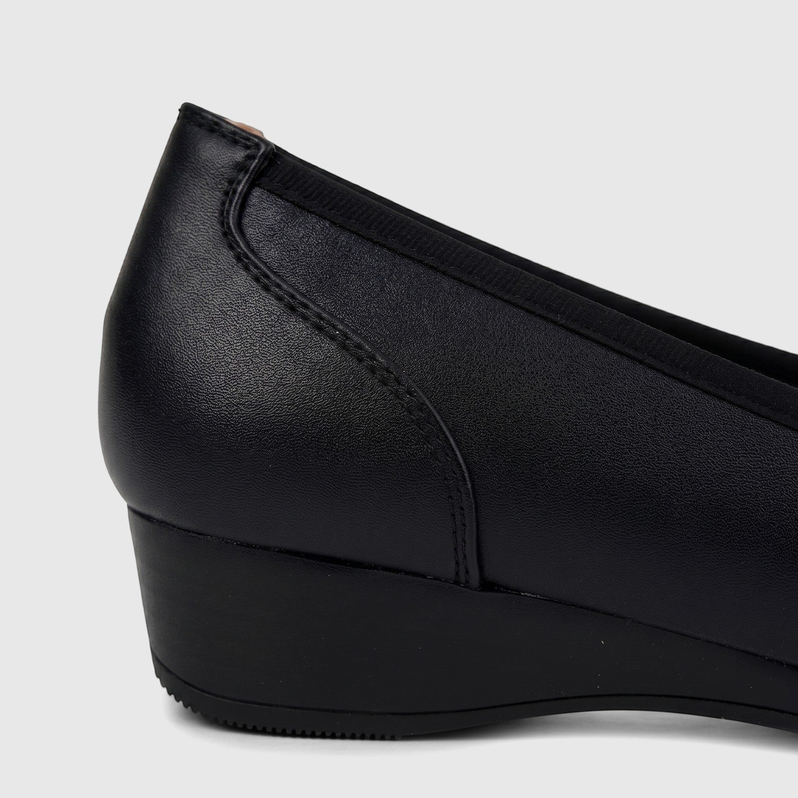 Close-up side view of a black leather Hush Puppies comfort wedge pump, showcasing its textured material and heel design.