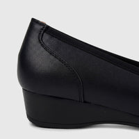 Close-up side view of a black leather Hush Puppies comfort wedge pump, showcasing its textured material and heel design.