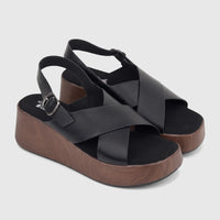A pair of black Hush Puppies Jemma comfort wedge sandals with criss-cross straps and dark brown faux wood soles, angled.