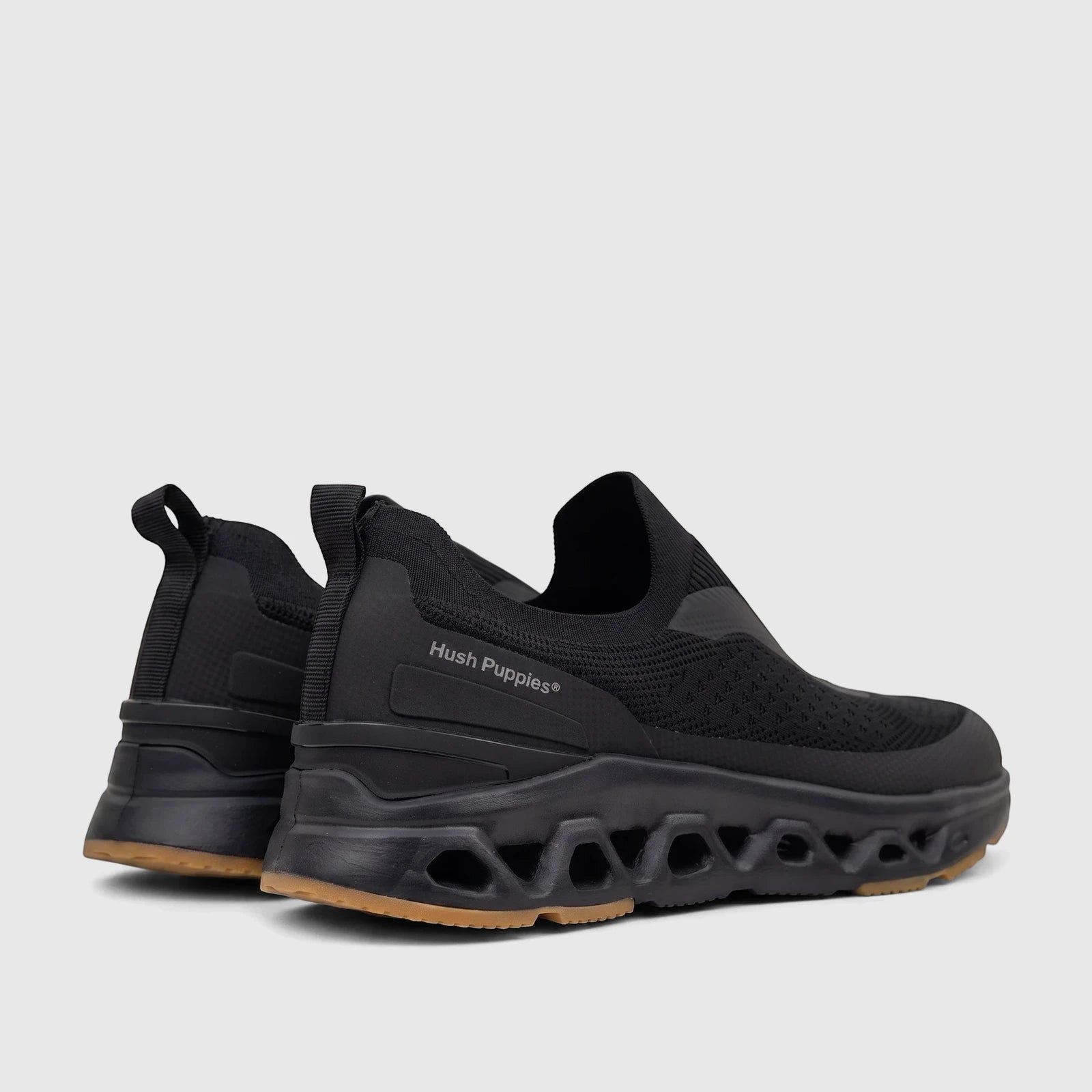 Pair of black Hush Puppies Men's Knoxx comfort slip-on sneakers with brown soles and a distinct hexagonal patterned midsole,