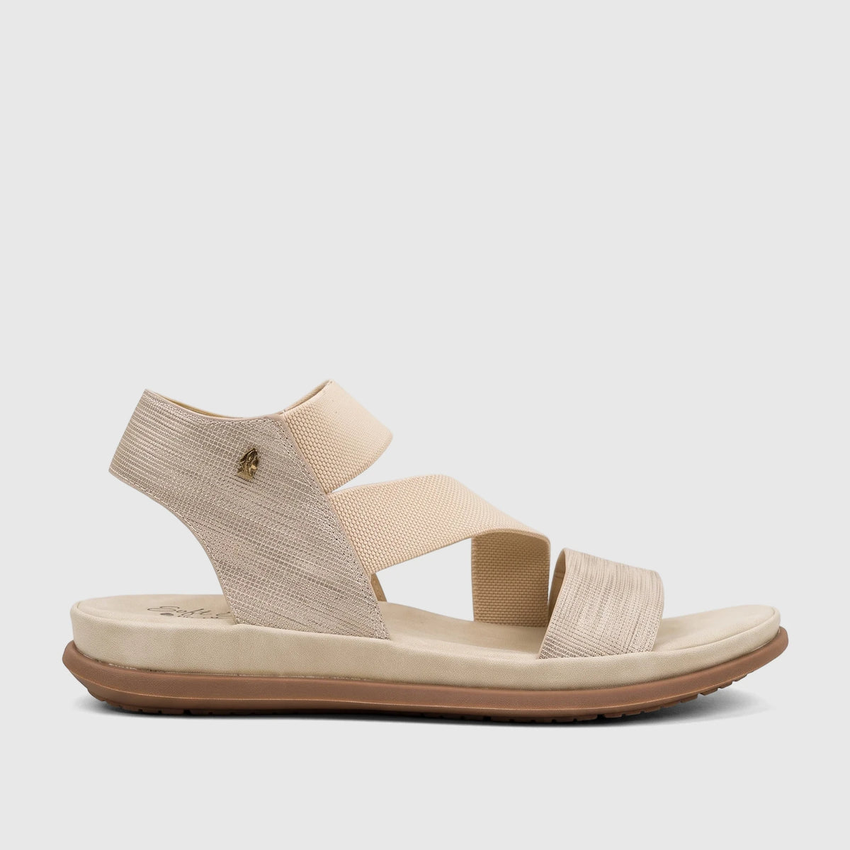Light gold Hush Puppies Soft Style Indy comfort sandal with elastic and shimmery straps, cushioned footbed, and brown sole.