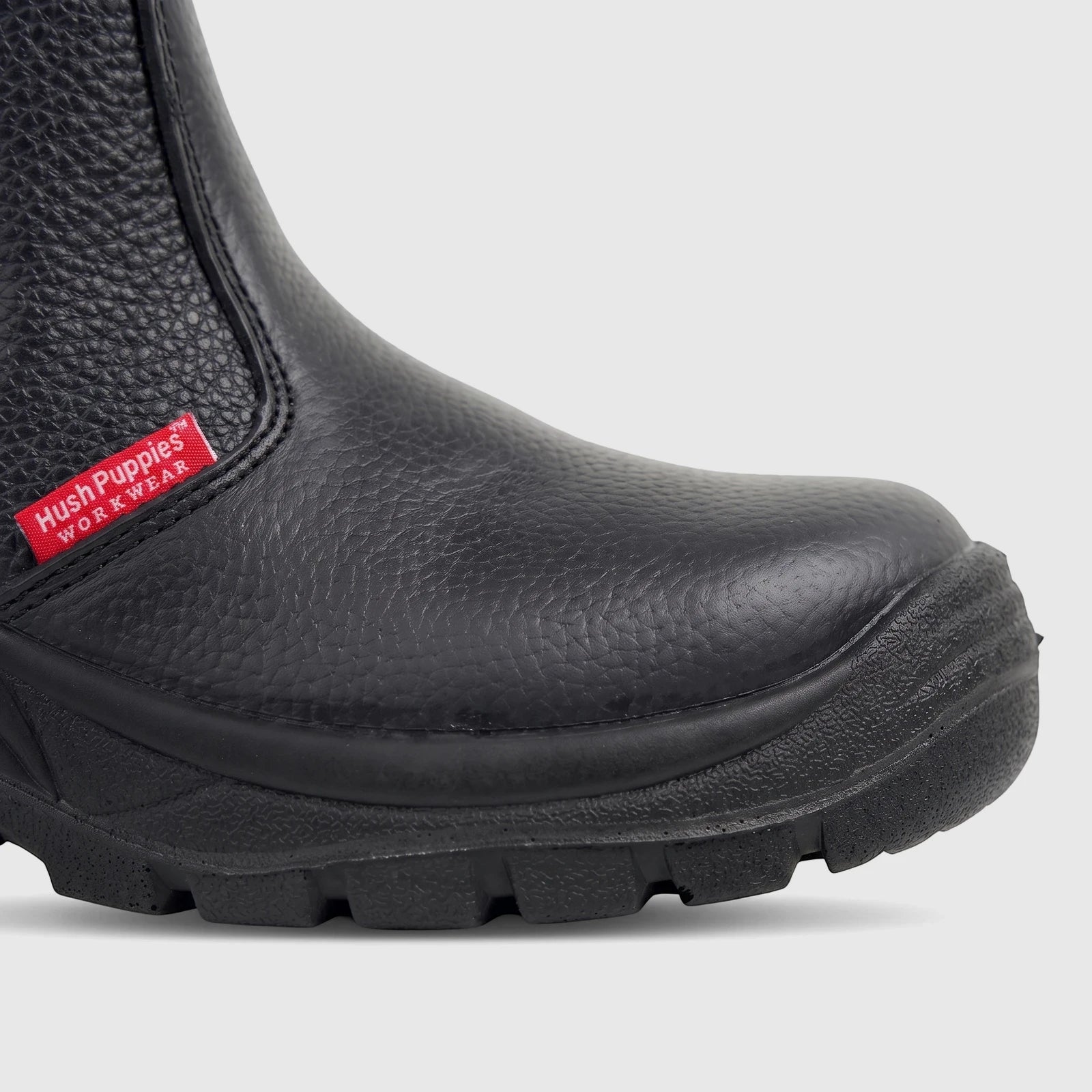 Close-up of a black Hush Puppies Unisex Safety Boot with a steel toe and textured workwear upper, showing the red brand