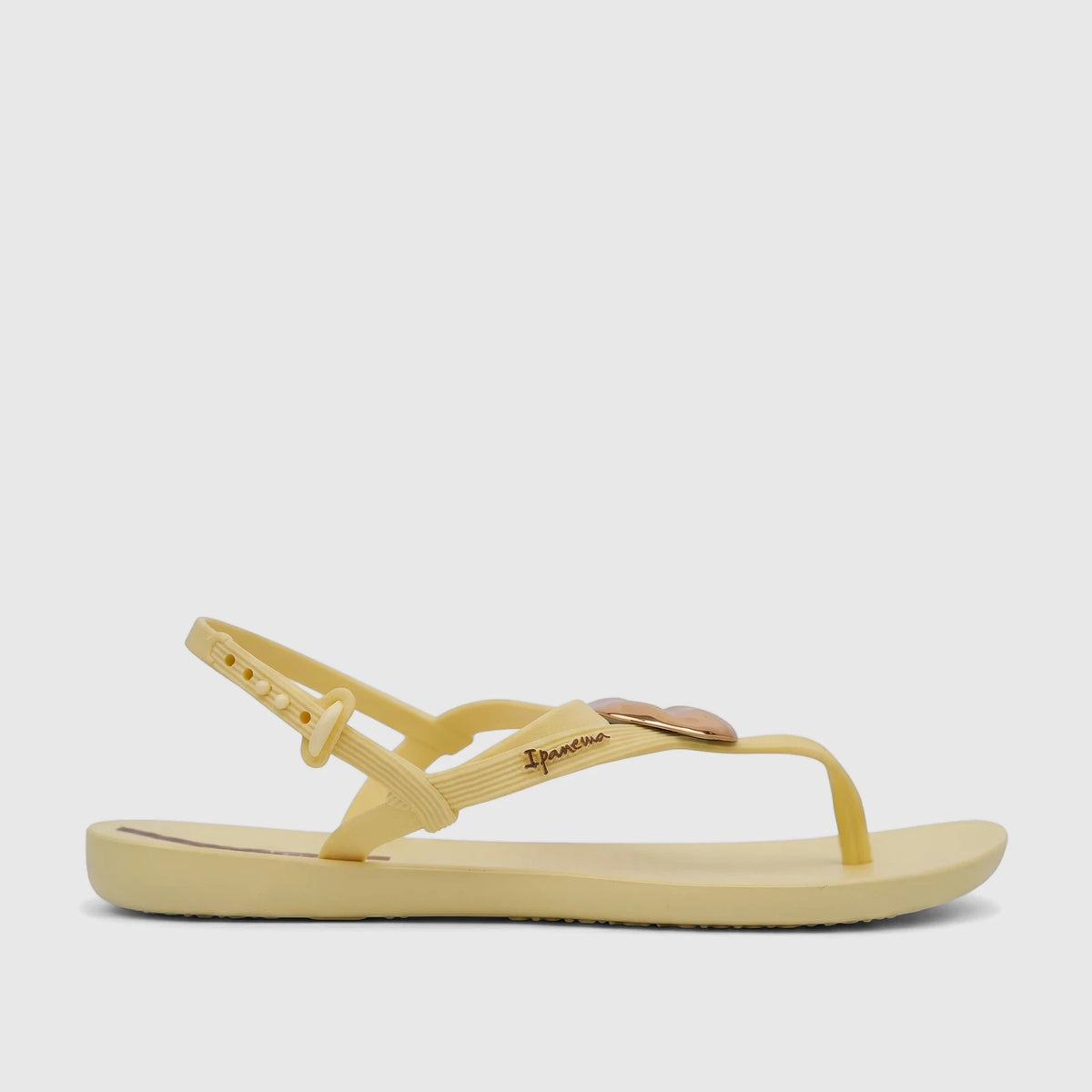 A side view of a yellow Ipanema Class Daring sandal with gold heart detail and an adjustable ankle strap.