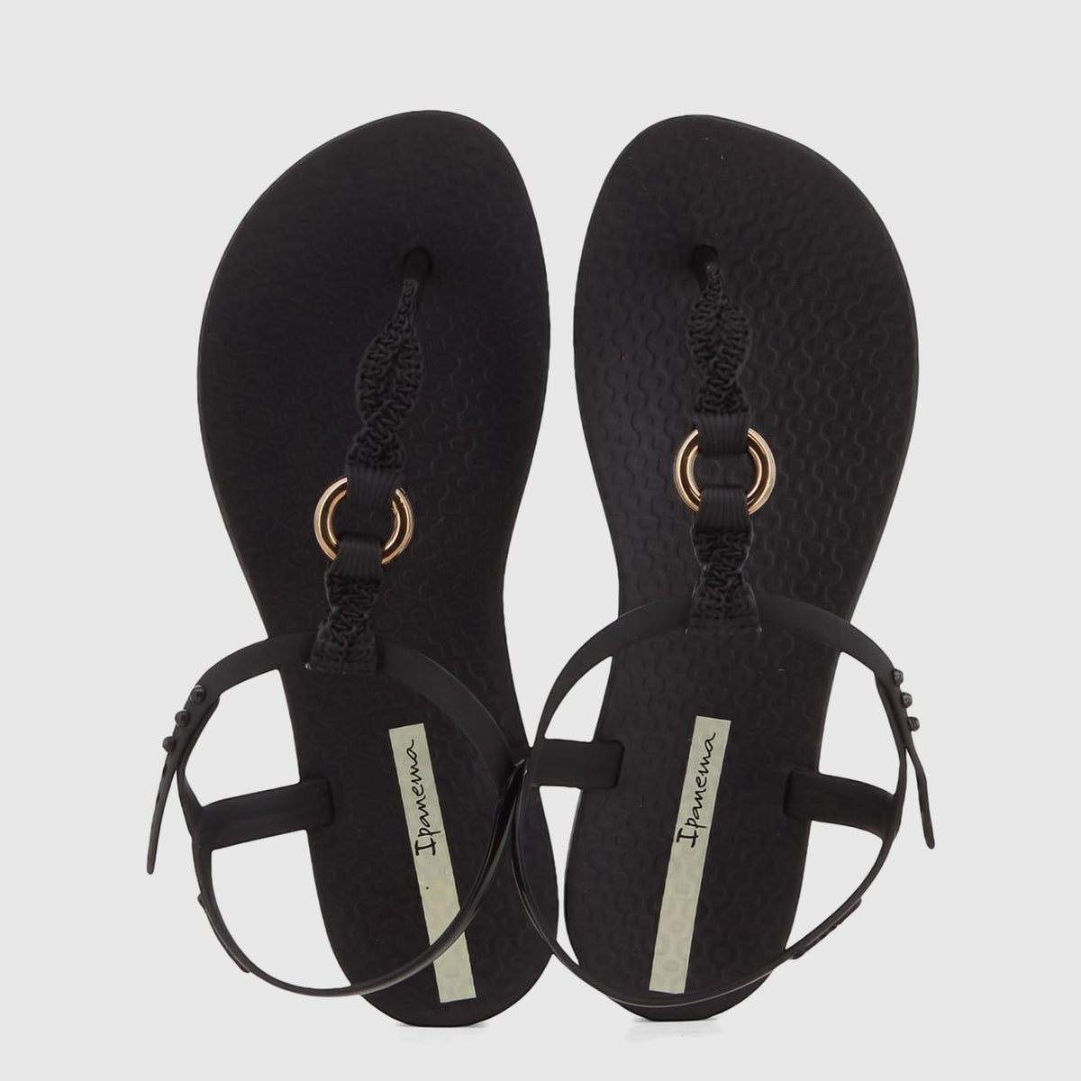 A pair of black Ipanema Class Luma GIL27428 sandals, featuring gold O-ring details and braided t-straps, presented from a