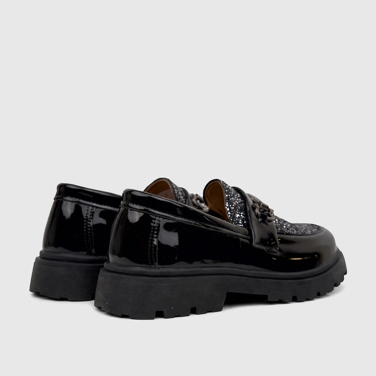 Pair of Klevas Boys Youth chunky sole loafers in black patent leather with silver glitter vamp and metal chain detail, seen