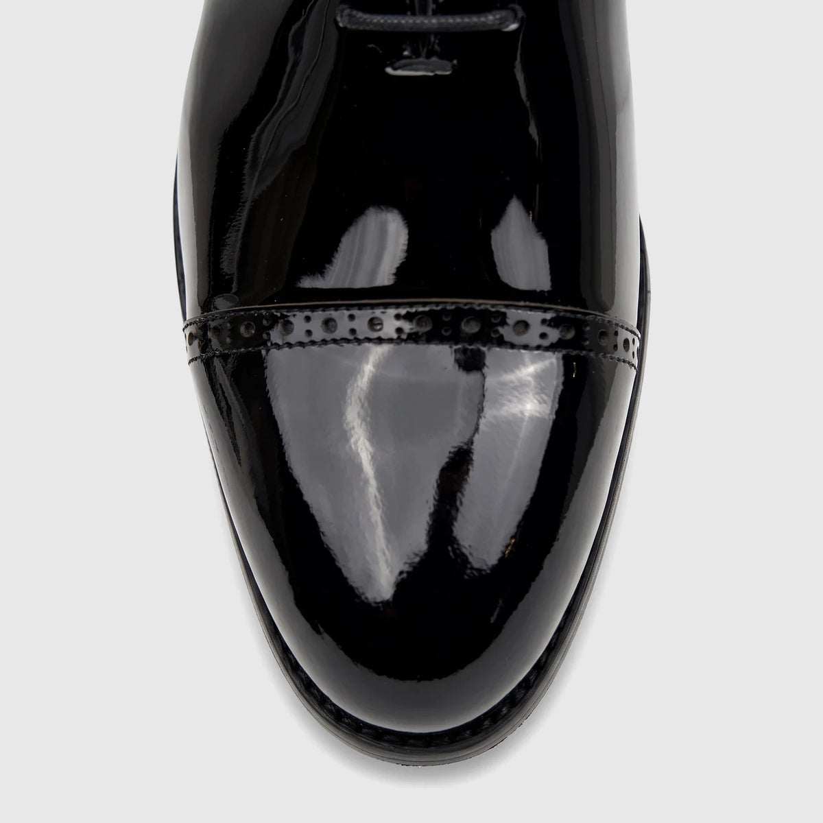 Men's black patent leather lace-up dress shoe, close-up of the polished toe cap with classic brogue detailing.