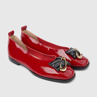 A pair of shiny dark red patent leather women's ballet flats with black bow-like ornaments and gold hardware on the toes.
