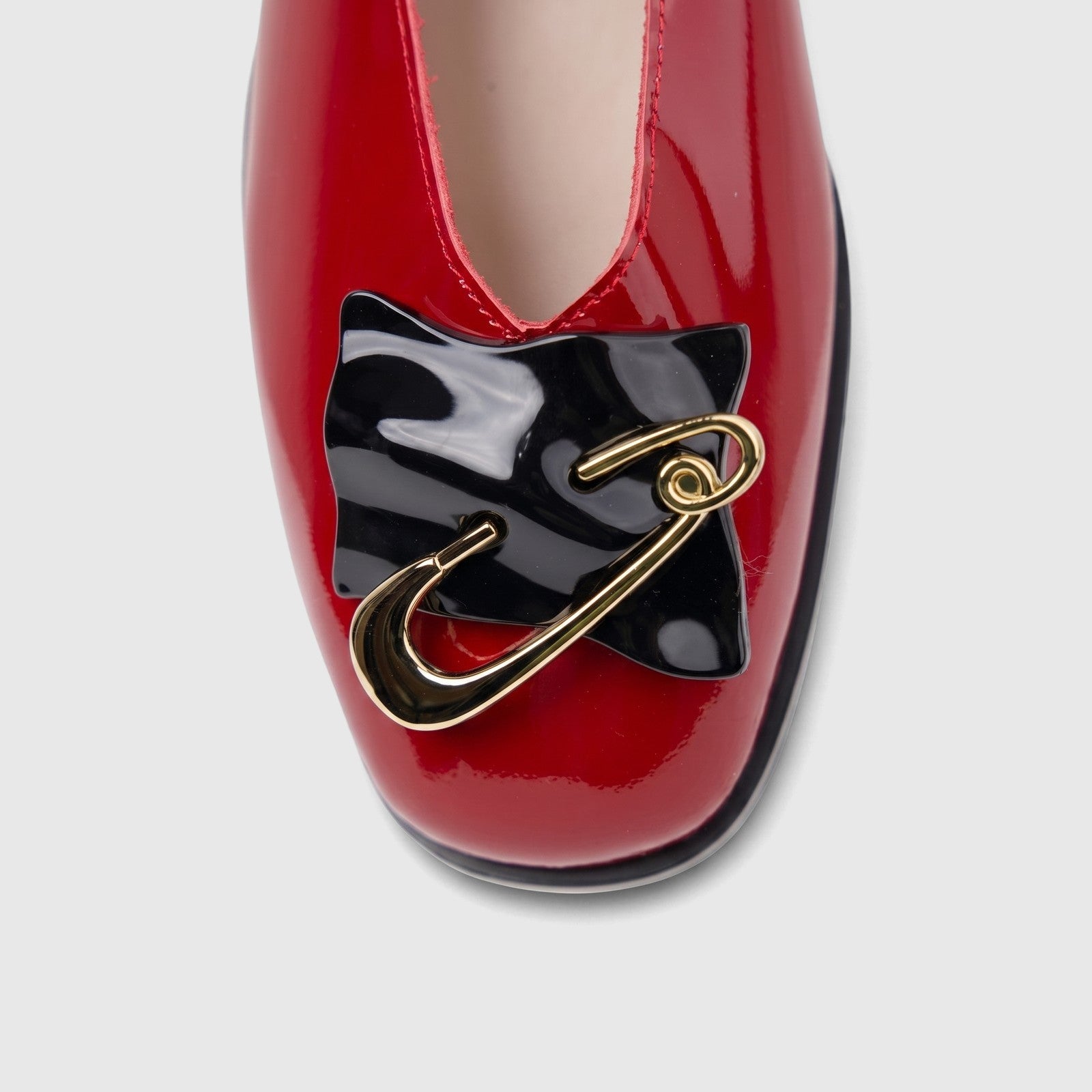 Close-up of a dark red patent leather Morbido ladies pump featuring a black bow and gold safety pin embellishment.