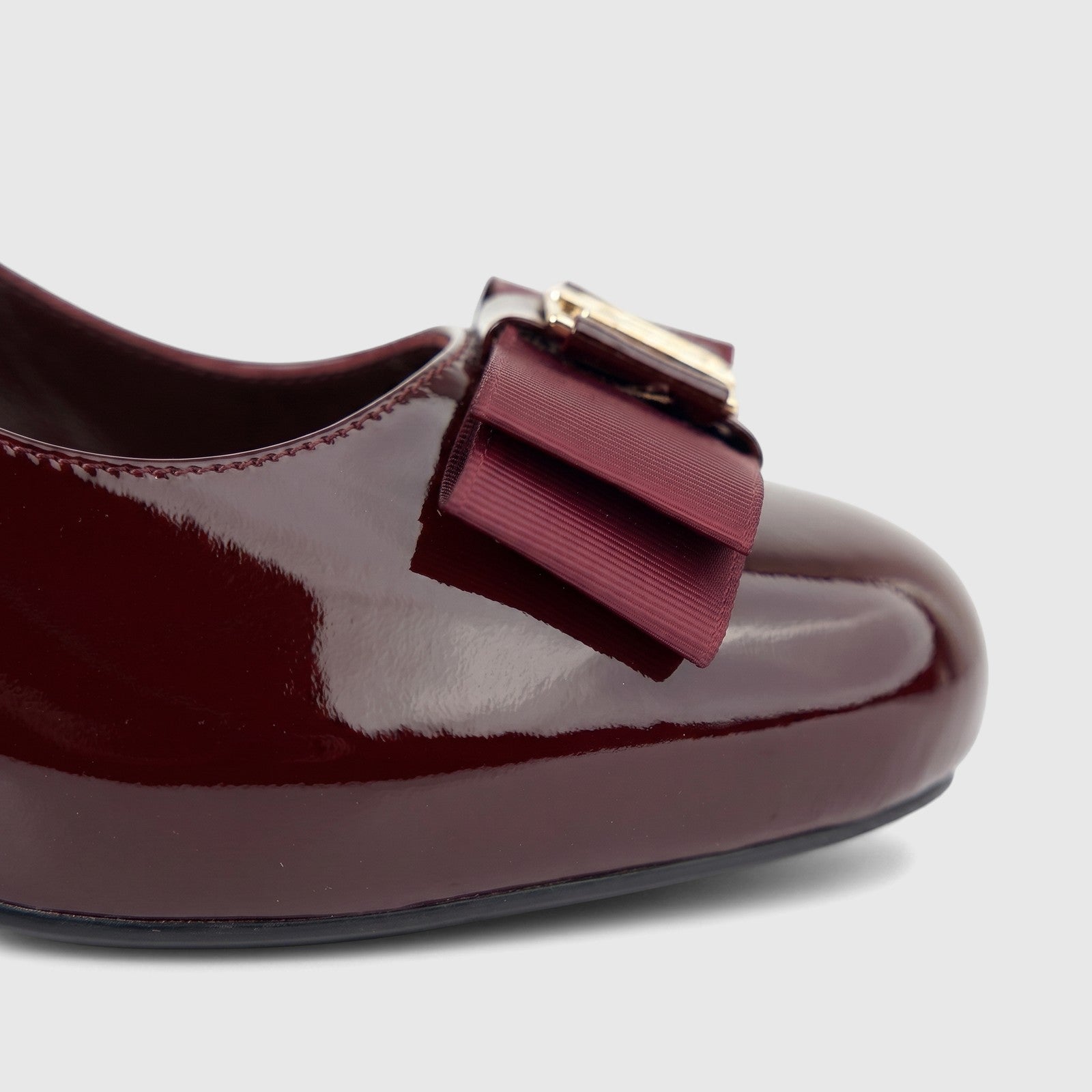 Close-up of a glossy wine red patent leather ladies' dress court shoe with a grosgrain ribbon bow and gold accent.