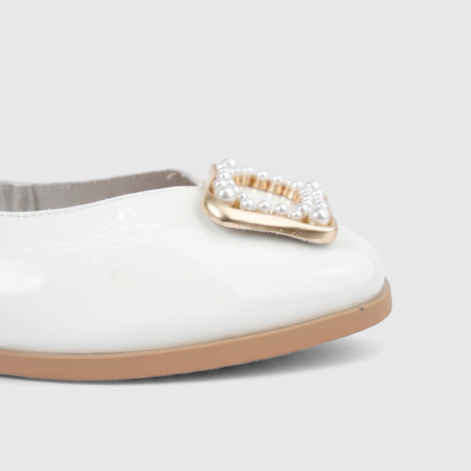Close-up of a white patent leather ladies pump shoe with a gold buckle embellished with white pearls on the toe.