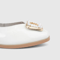 Close-up of a white patent leather ladies pump shoe with a gold buckle embellished with white pearls on the toe.