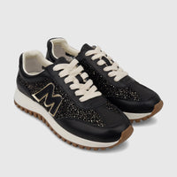 A pair of Morbido black leather women's sneakers with gold glitter panels, cream laces, and a gold 'M' logo, displayed at an