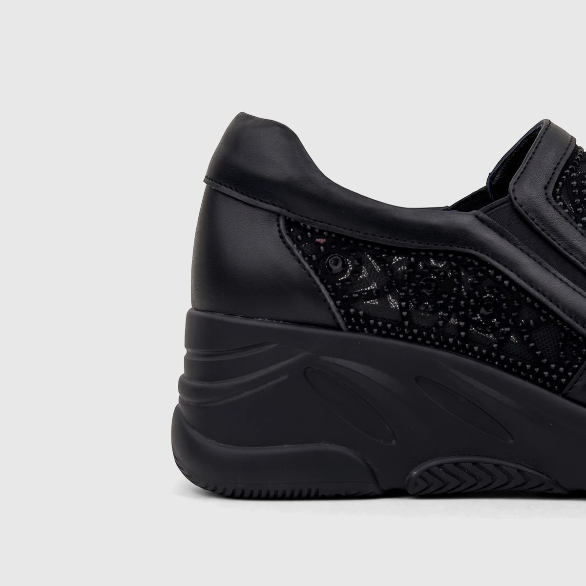 Black leather wedge sneaker with delicate lace-like pattern and stud details, visible from the heel to mid-foot.