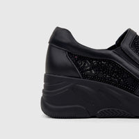 Black leather wedge sneaker with delicate lace-like pattern and stud details, visible from the heel to mid-foot.