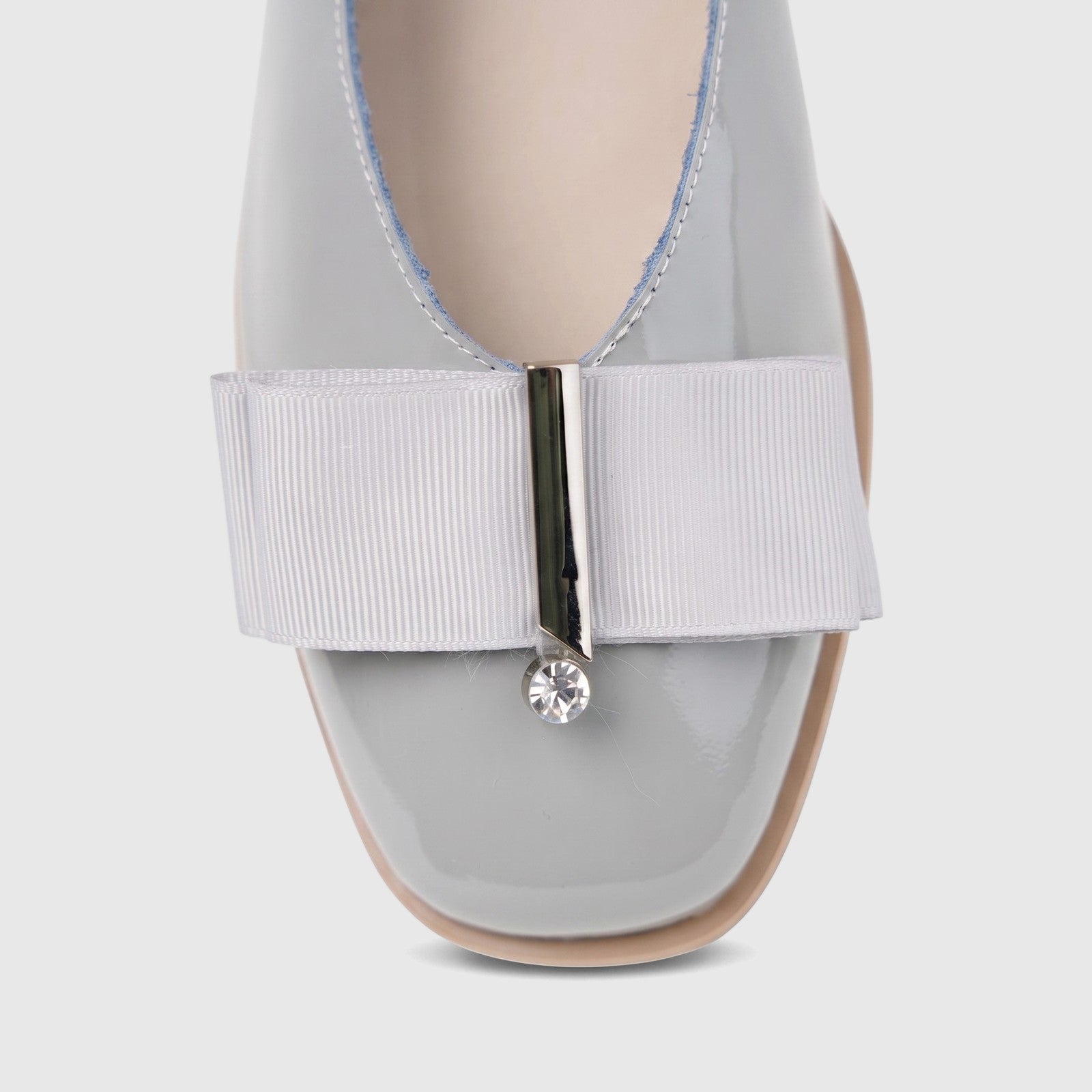 Close-up of a light grey patent leather women's pump with a square toe, featuring a ribbon bow and a small crystal detail on
