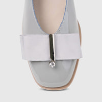 Close-up of a light grey patent leather women's pump with a square toe, featuring a ribbon bow and a small crystal detail on