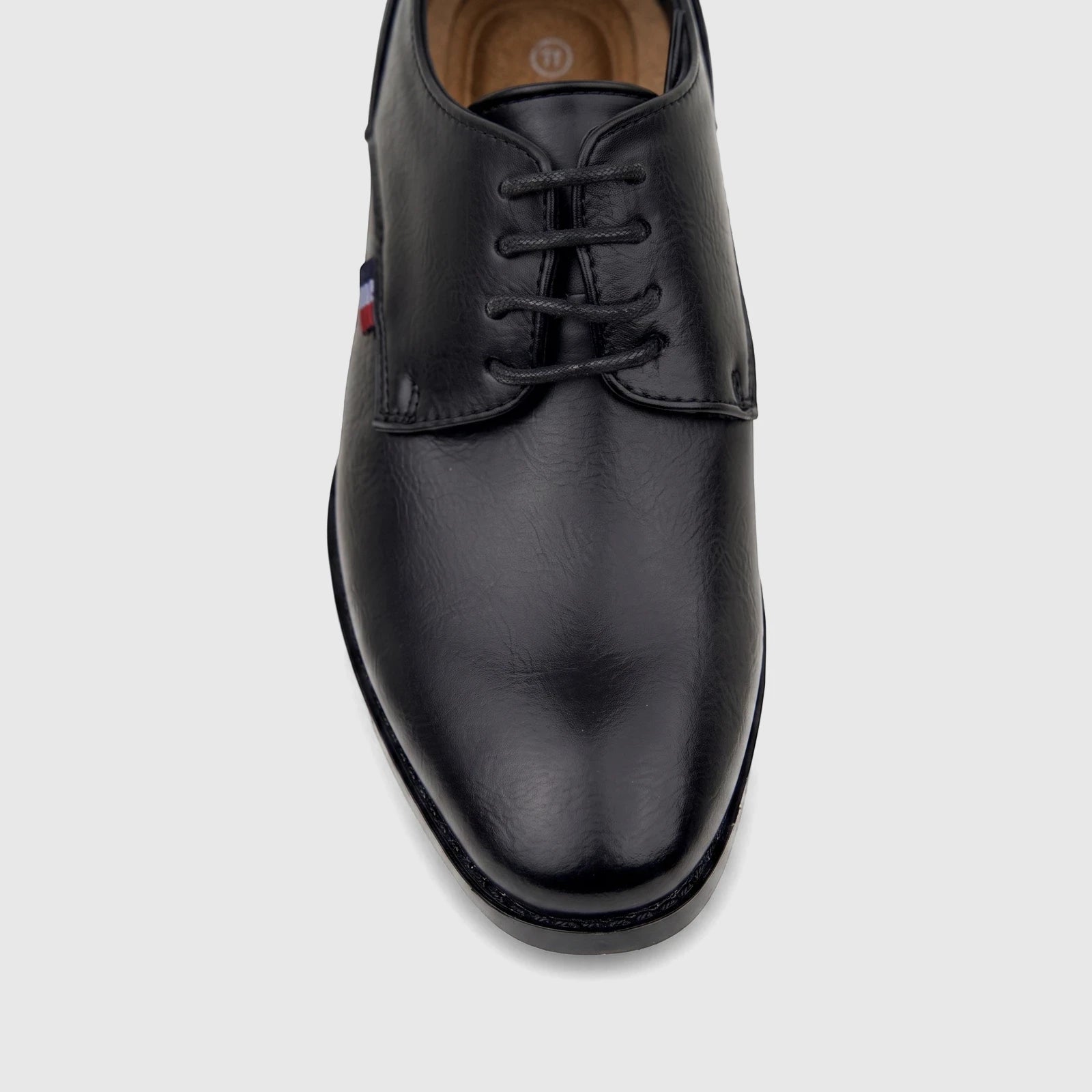 Black boys' dress lace-up shoe with a small flag logo on the side, presented on a clear stand.