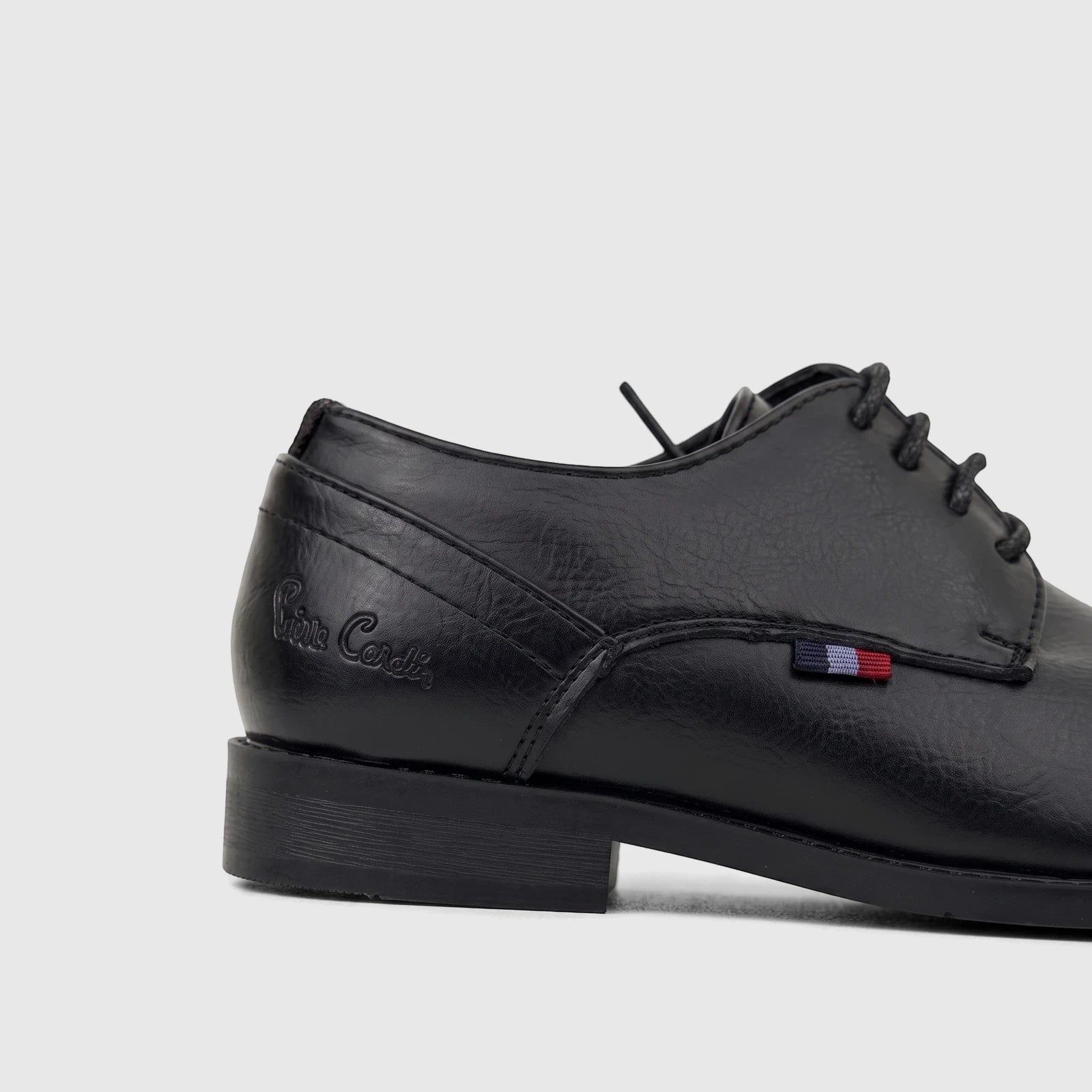 Side view of a black boys' dress lace-up shoe with textured leather and a small striped tag on a white background.
