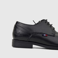 Side view of a black boys' dress lace-up shoe with textured leather and a small striped tag on a white background.